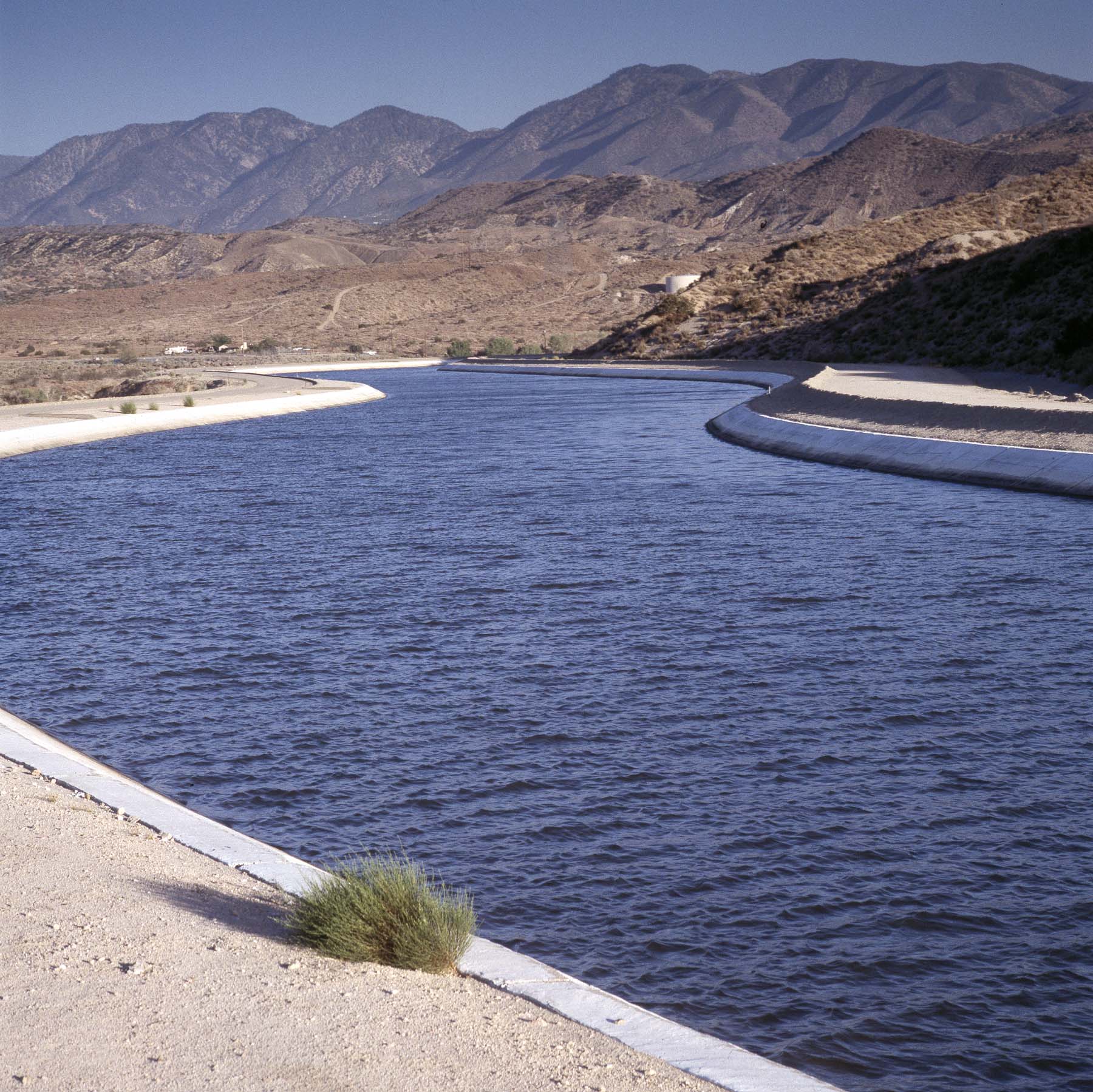 A photo showing a canal with water and mountains in the background.