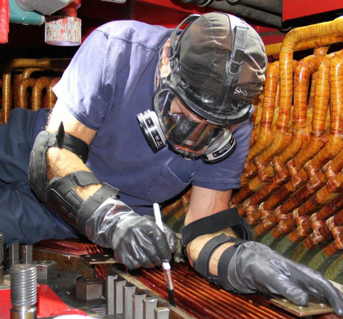 An employee wearing a protective mask and gloves works on copper bus bars.