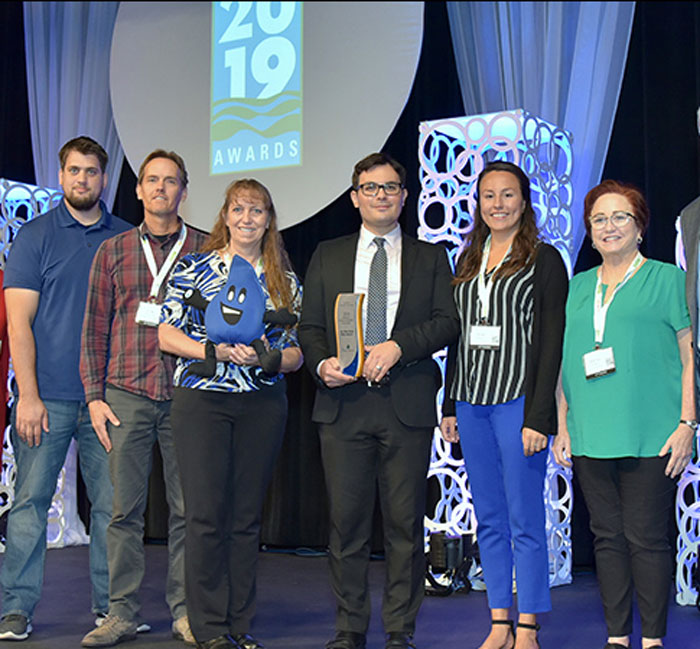 Several water industry professionals stand on a stage holding an award.