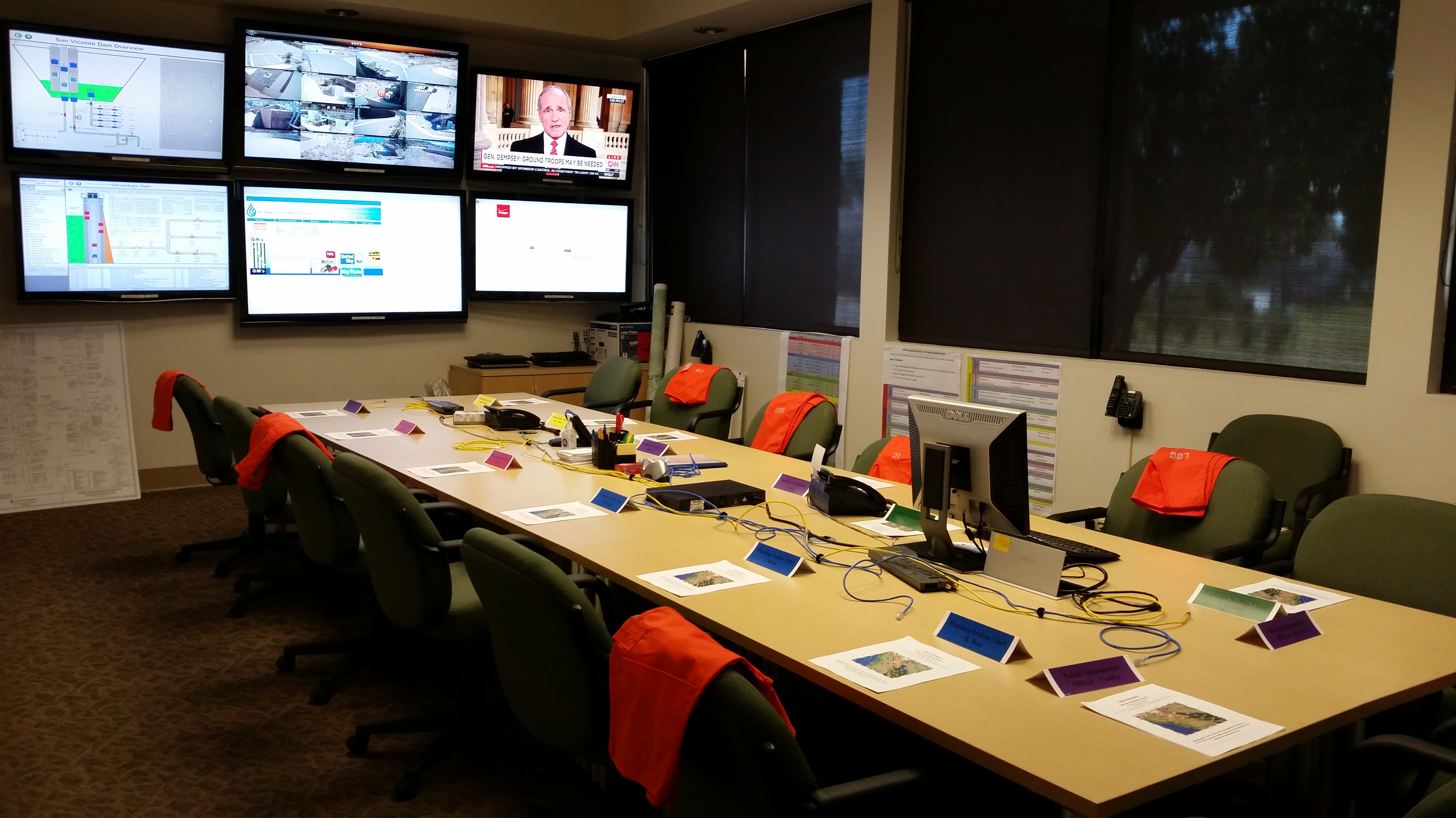 A conference room with several screens mounted on the walls, phones set up for emergency calls and information sheets and name cards at a large table.
